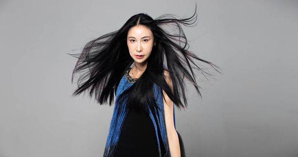 Azjatka Transgender Kobieta z długimi czarnymi prostymi włosami, wiatr wieje w powietrze. Kobieta spin obrócić się i nosić niebieski moda zmysłowy sexy sukienka, szary tło izolowane przestrzeń kopia - Zdjęcie, obraz