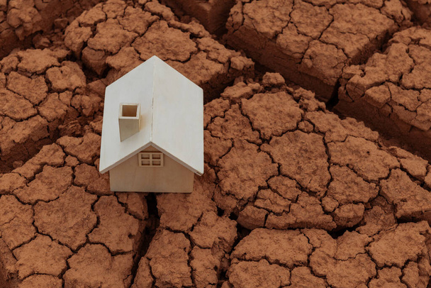 Simbolico casa in legno si erge su argilla secca incrinata - Foto, immagini