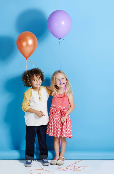 Daj się ponieść emocjom. Portret uroczej dziewczynki i chłopca trzymających balon na niebieskim tle - Zdjęcie, obraz