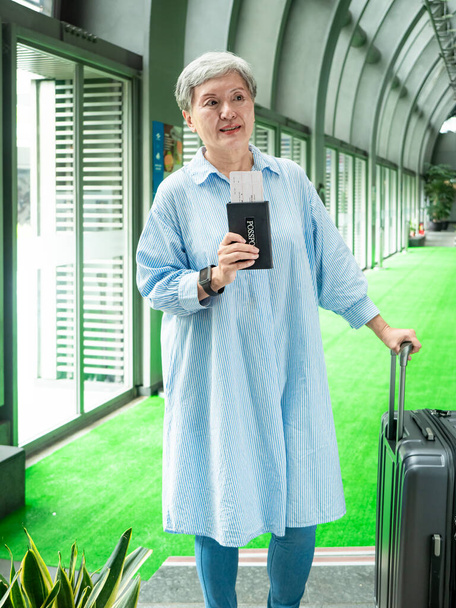 Muotokuva vanhempi aikuinen vanhusten aasialainen nainen 60s hymyillen kanssa matkalaukku matkatavaroiden laukku ja tilalla passi lippu matka käsite. - Valokuva, kuva