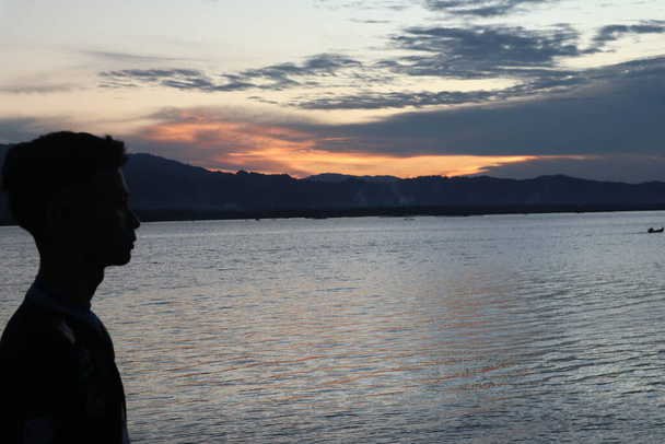 Siluetti nuoresta miehestä seisomassa järven rannalla nauttimassa auringonlaskusta. rauhallinen ilmapiiri luonnossa - Valokuva, kuva