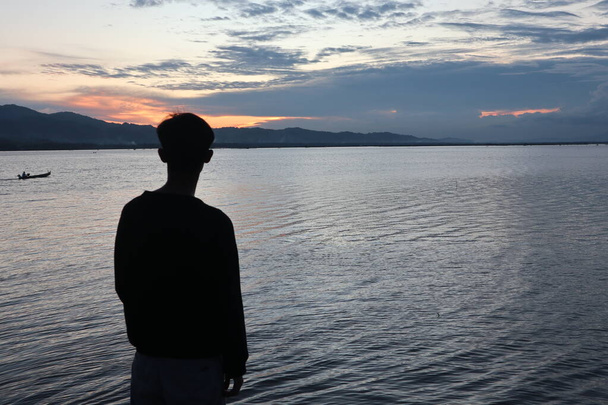 Silhouette di un giovane uomo in piedi vicino al lago godendo il tramonto. atmosfera tranquilla nella natura - Foto, immagini