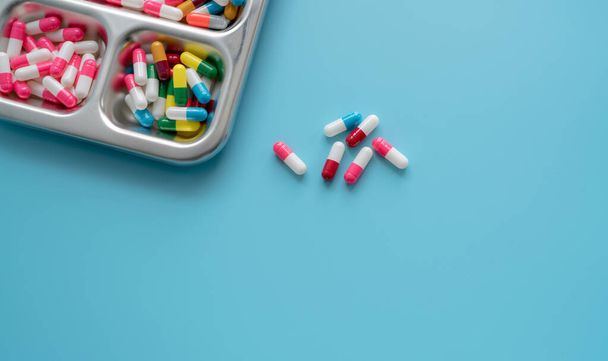 High-angle view van multi-gekleurde antibiotica capsule pillen op roestvrij stalen lade en blauwe achtergrond. Antibioticaresistentie. Medicijnen op recept. Farmaceutische industrie. Gezondheidszorg en geneeskunde. - Foto, afbeelding