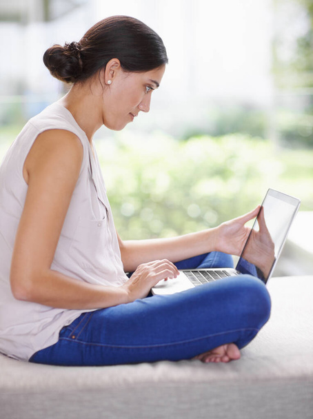 My wifi lets me browse anywhere I want. an attractive young woman using a laptop while relaxing at home - Foto, imagen