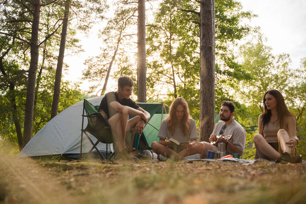 Compañía de amigos excursionistas acampando juntos en verano tocando la guitarra y bebiendo té. - Foto, imagen
