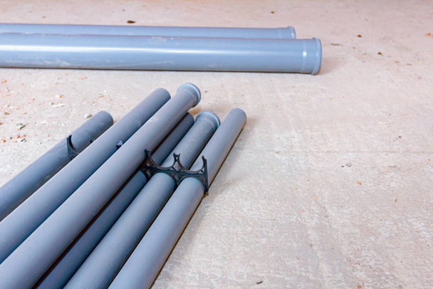 Un sacco di nuovi tubi fognari idraulici grigi sono disposti sul pavimento in attesa di essere installati in un edificio in costruzione. - Foto, immagini