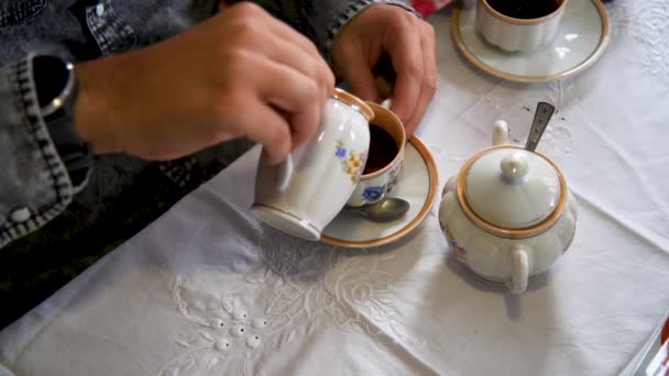Close-up van interraciale jonge paar handen bereiden en drinken van een koffie met melk en suiker met behulp van een vintage porseleinen kopje met bloemen patroon. - Video