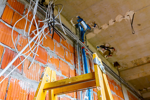 Drabinki ułatwiające instalację kabli, skrzynki rozdzielcze na prąd. Kable zwisają z sufitu, przechodząc między piętrami w budynku w trakcie budowy.. - Zdjęcie, obraz