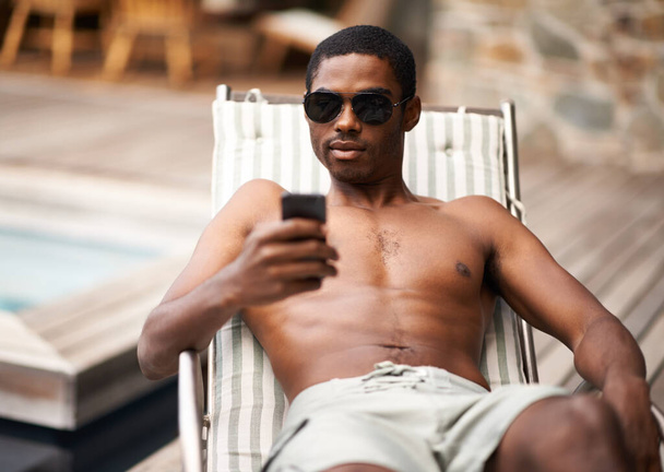 Status updates to make you jealous. A young black man reclining on a deck chair by the pool - Photo, Image