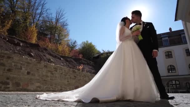 Γάμος ζευγάρι με ένα μπουκέτο λουλούδια στα χέρια τους με φόντο το ηλιοβασίλεμα, η νύφη και ο γαμπρός, αγκαλιάζουν τρυφερά και φιλάνε - Πλάνα, βίντεο