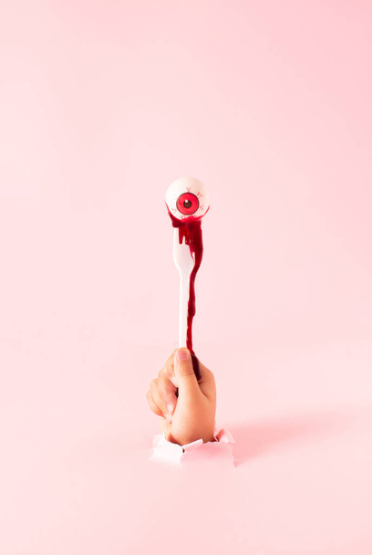 Blood from the eyeball drips down the hand. Creative scary Halloween concept. - Foto, afbeelding
