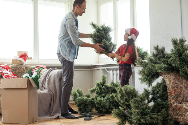 Father and daughter assembling christmas tree, smiling - christmas, holiday, winter concept, family activity - Photo, Image