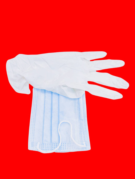 Gezichtsmasker en chirurgische latex beschermende handschoen bij elkaar gehouden voor de bescherming van handen en huid dekking mond neus van coronavirus covid19 en andere ziekten geïsoleerd op rode achtergrond closeup beeld bekijken foto - Foto, afbeelding