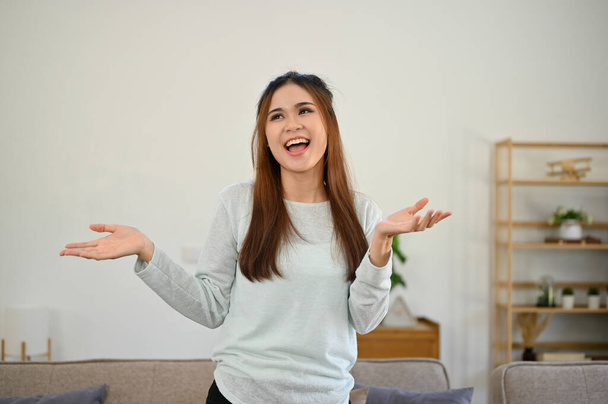 Joyful and happy young Asian woman in casual outfit having a great time at home on her day off, smiling and dancing in her living room. - Foto, Bild