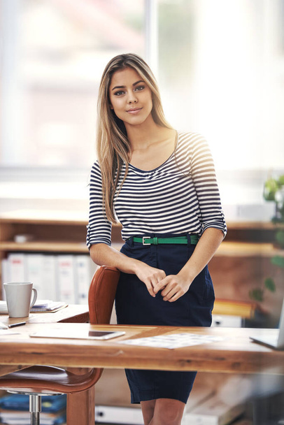 Пожалуйста, проходите и садитесь. Обрезанный портрет молодой предпринимательницы, стоящей за столом в офисе - Фото, изображение
