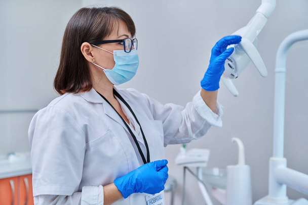 Serious confident female doctor dentist in face mask in dental office, profile view. Dentistry, medicine, specialist, career, dental health care concept - Foto, Imagem
