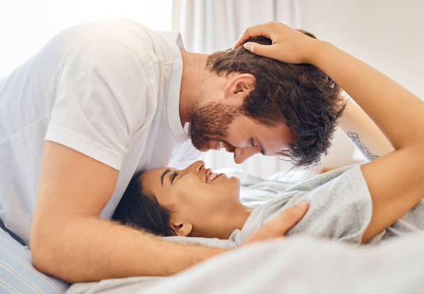 Couple, love and happy with a man and woman in bed in the bedroom of their home together with a smile. Romance, dating and affection with a young male and female bonding and being intimate in a house. - Photo, Image