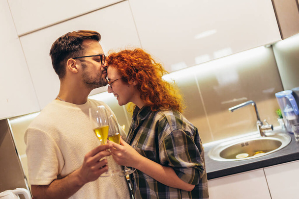 Cute young couple drinking wine in kitchen. - Foto, imagen