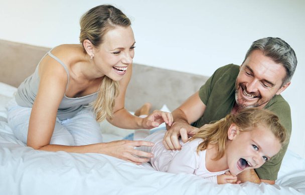 Ευτυχισμένη οικογένεια, κρεβάτι και διασκεδαστική οικογένεια παίζοντας και γελώντας χαλαρώνοντας με το κοριτσάκι σε ένα υπνοδωμάτιο. Ευτυχισμένοι, παιχνιδιάρηδες και στοργικοί γονείς να είναι ανόητοι με ενθουσιασμένο παιδί, απολαμβάνοντας ελεύθερο χρόνο στο σπίτι τους. - Φωτογραφία, εικόνα