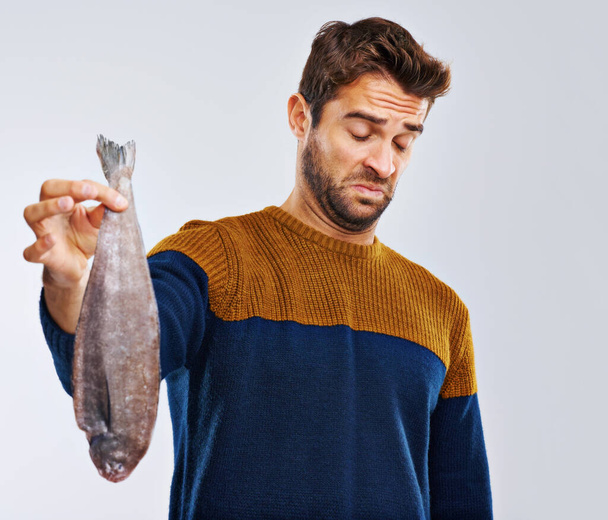 I hope it tastes better than it smells. Studio shot of a man showing disgust while holding a smelly fish - Foto, imagen