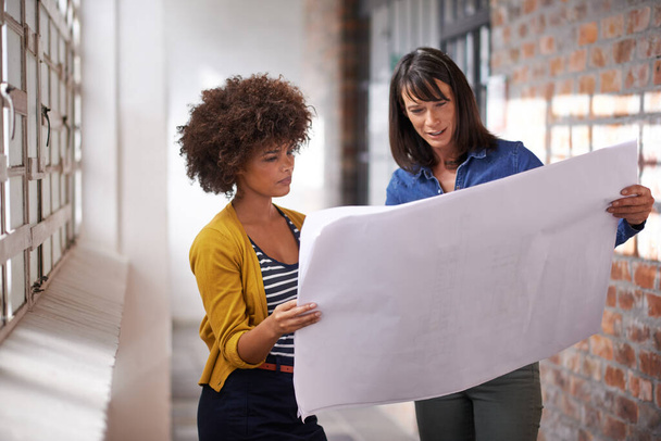 It all comes together with a good plan. two female architects discussing blueprints while standing inside a building - Foto, Imagem