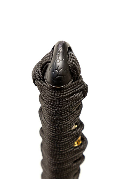 Close up the Kashira: butt cap (or pommel) made of steel on the end of the black silk cord wrapped handle Japanese sword isolated in white background. Selective focus. - Foto, immagini