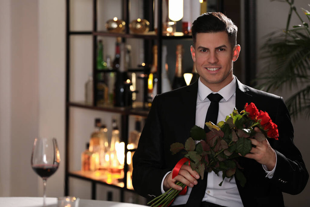 Happy man with roses waiting for his girlfriend in restaurant on Valentine's day - Fotografie, Obrázek