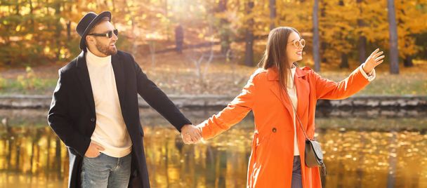 Happy young couple holding hands in beautiful autumn park near lake - Photo, Image
