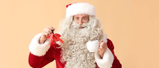Weihnachtsmann mit Weihnachtsglocke und Tasse Kakaogetränk auf beigem Hintergrund - Foto, Bild