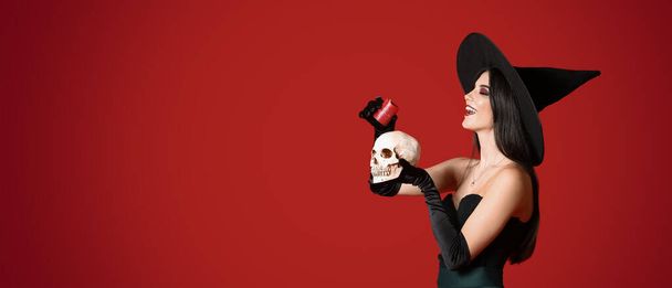 Jovem bruxa segurando crânio e vela no fundo vermelho com espaço para texto - Foto, Imagem