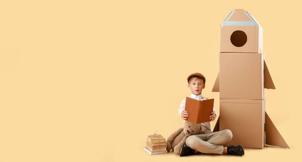 Překvapený chlapeček s knihami, hračkou a lepenkovou raketou na béžovém pozadí s prostorem pro text - Fotografie, Obrázek