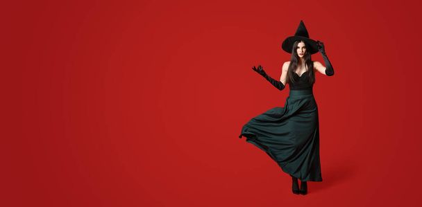 Beautiful woman dressed as witch for Halloween on red background with space for text - 写真・画像