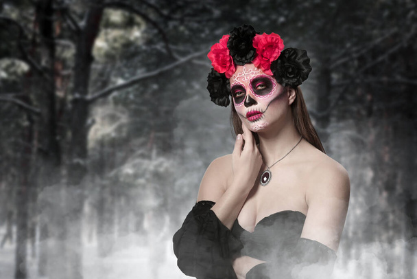 Young woman with painted skull on her face for Mexico's Day of the Dead in forest - Foto, Bild