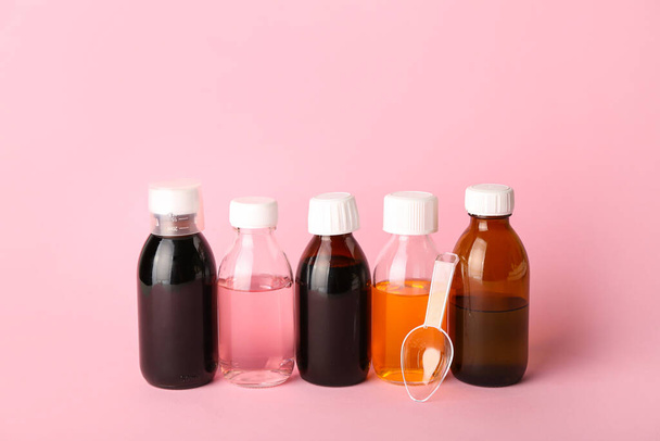 Пляшки сиропу і ложки кашлю на рожевому фоні
 - Фото, зображення