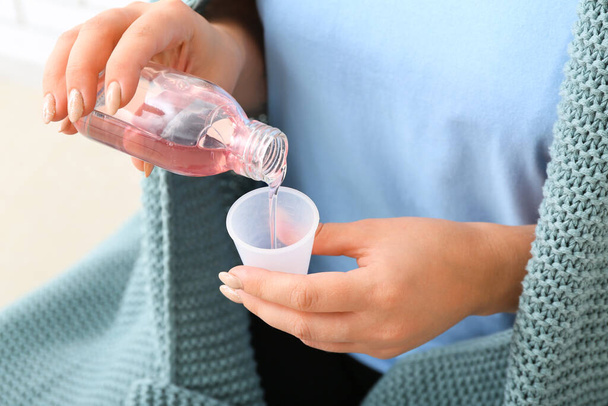Mulher derramando xarope de tosse do frasco em copo no fundo branco, close-up - Foto, Imagem