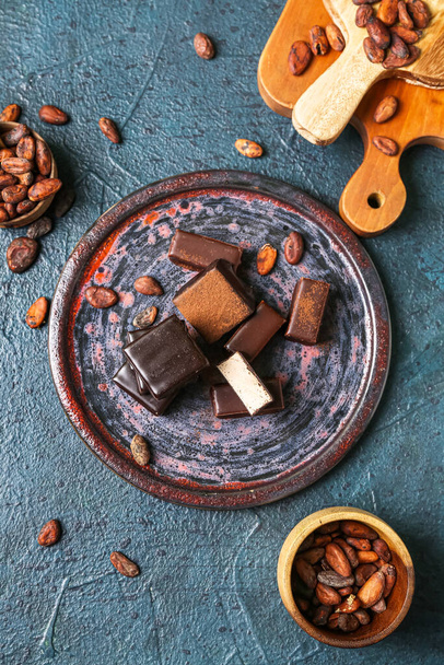 Composition with plate of tasty bird's milk candies and cocoa beans on dark color background - Photo, Image