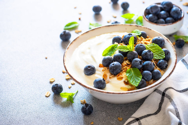 Griechischer Joghurt mit Müsli und Blaubeeren am hellen Küchentisch. - Foto, Bild