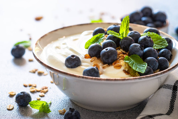 Greek Yogurt with granola and blueberies at light kitchen table. - Valokuva, kuva