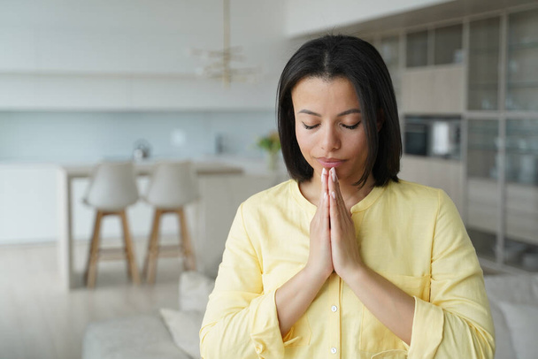Serene young woman practice yoga, meditating, breathing folded hands in namaste gesture at home. Calm female praying with closed eyes. Healthy lifestyle, meditation, stress relief concept. - Photo, Image
