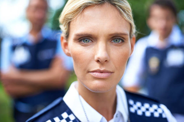 Διατηρώντας την ειρήνη. μια σοβαρή αστυνομικός με τους συναδέλφους της στο παρασκήνιο - Φωτογραφία, εικόνα