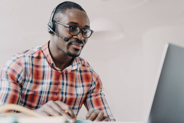 Fókuszált afro-amerikai férfi támogató munkás fejhallgatót visel, a laptopnál dolgozik, kommunikál az ügyféllel. Fekete férfi call center operátor tanácsadás ügyfél online. Távmunka-koncepció. - Fotó, kép