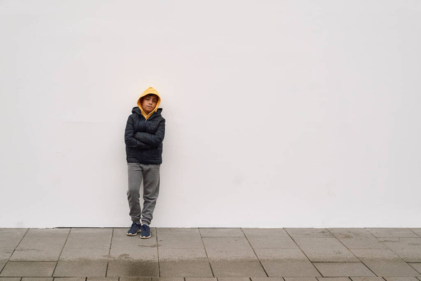 Kleiner modischer Junge posiert vor weißer Betonwand. Konzept von Stil und Mode für Kinder. - Foto, Bild