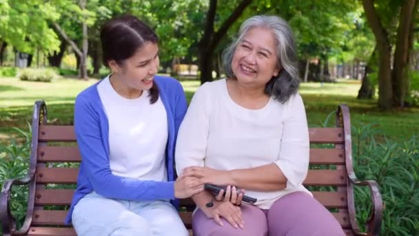 Happy senior mother with gray hair talk and laugh with daughter or caregiver in the park. Concept of happy retirement with care from a caregiver and Savings and senior health insurance, senior care - Кадры, видео