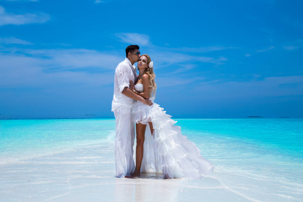 Summer love. Beautiful happy young couple in wedding clothes is standing on a beach in the Maldives. Engagements and wedding on the beach on the paradise island of Maldives. Luxury travel. - Foto, Imagem