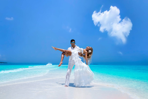 Sommerliebe. Ein schönes, glückliches junges Paar in Hochzeitskleidung steht an einem Strand auf den Malediven. Verlobungen und Hochzeiten am Strand der paradiesischen Insel Malediven. Luxusreisen. - Foto, Bild