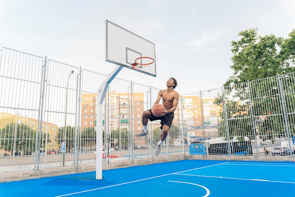 Unrecognized african boy wearing sports clothes playing basketball and throwing the ball. - Foto, Bild