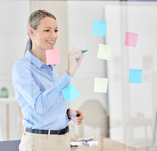 Schreiben, Planen und Denken mit klebrigen Zetteln auf einem Glas in einem modernen Büro. Glückliche Managerin, Führungspersönlichkeit oder Ceoplan-Strategie auf dem Papier in einem Marketing- und Werbeunternehmen. - Foto, Bild
