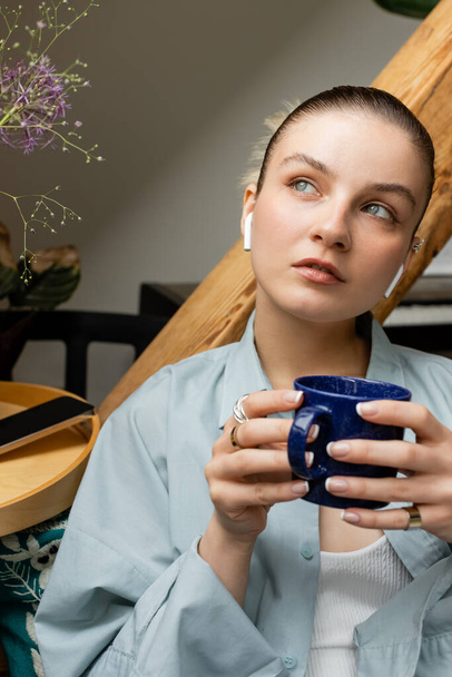 Молода жінка в навушниках тримає чашку і дивиться вдома
  - Фото, зображення