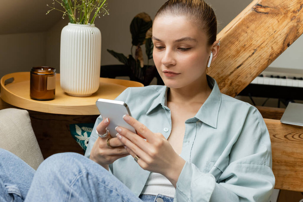 Mujer en auricular usando el teléfono celular en el sofá en la sala de estar  - Foto, imagen