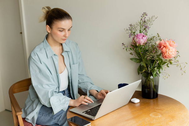 Young woman using laptop near cup and flowers at home  - Photo, Image